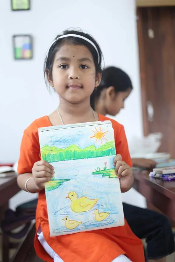 A young student proudly showing her drawing at DK Art & Craft Institute