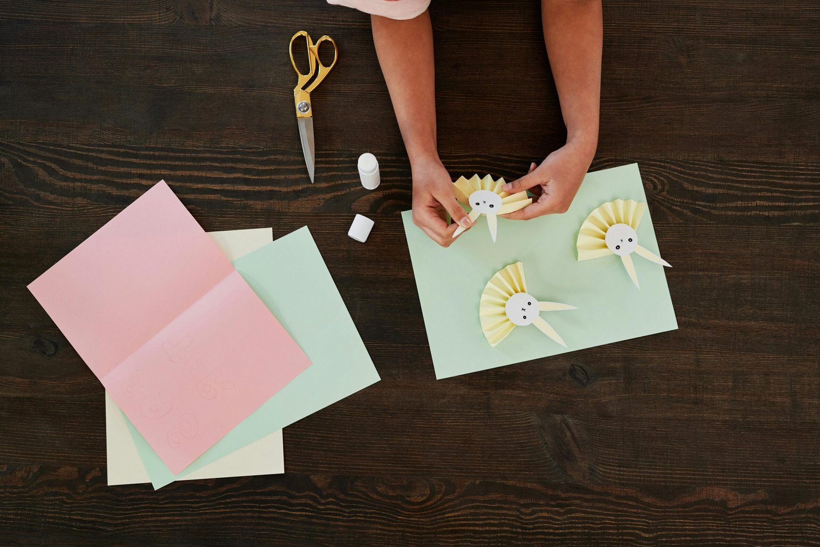 Overhead view of child creating Easter bunny crafts with colorful paper and scissors.