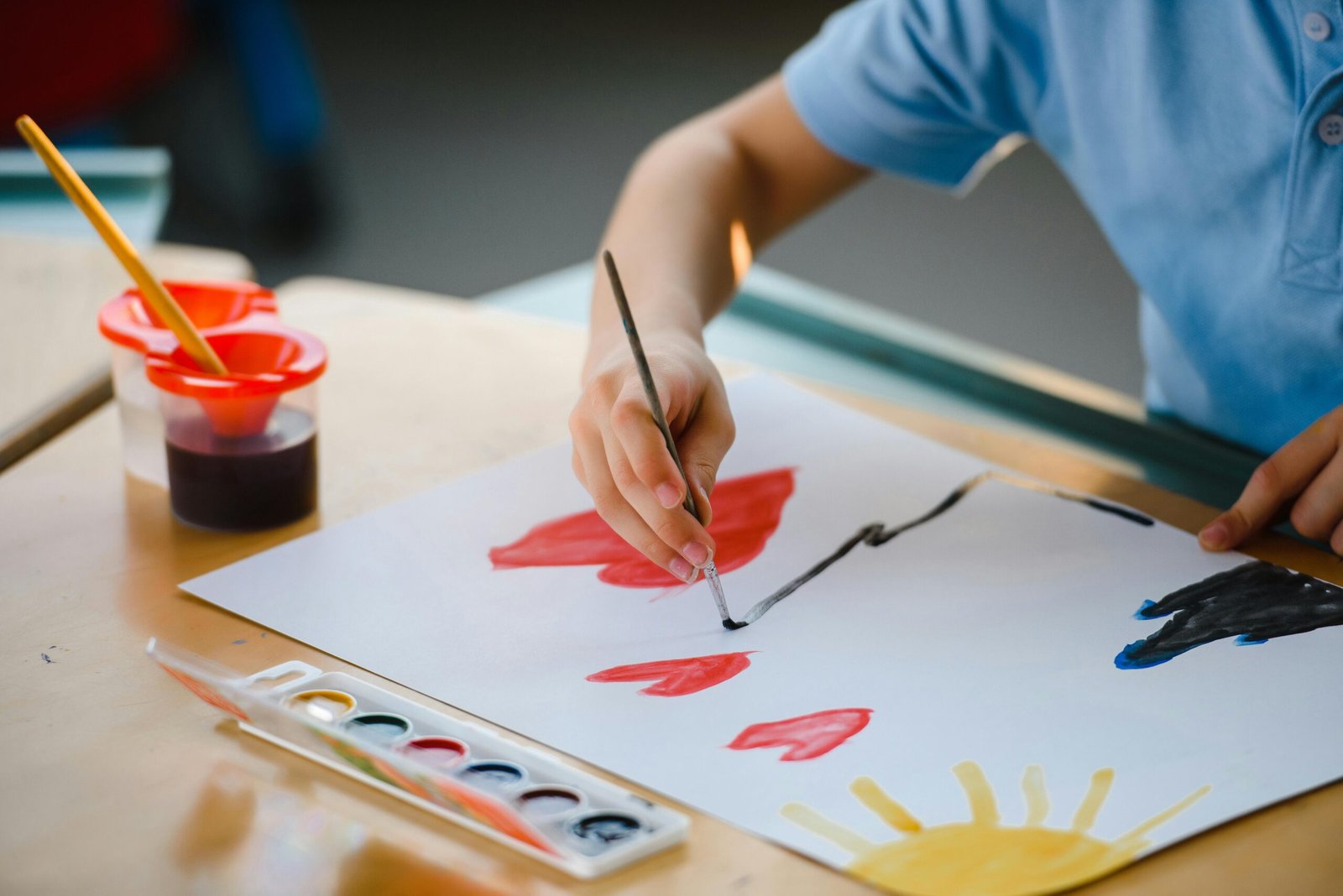 Young child using watercolors and brush to paint on paper indoors at a school setting.